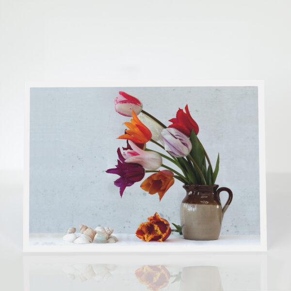 an arrangement of colourful tulips in an earthenware jug with shells and seaglass